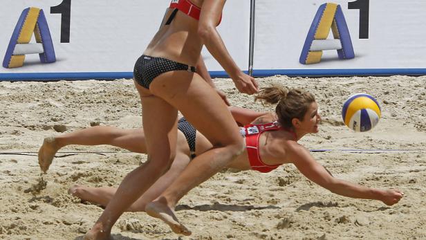 Eine Beachvolleyballspielerin hechtet nach dem Ball, während eine andere bereitsteht.