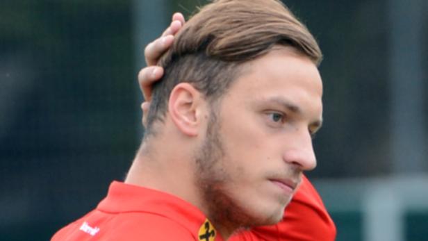 Ein Mann mit braunen Haaren und Bart berührt seinen Hinterkopf.