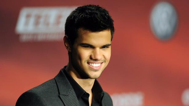Taylor Lautner lächelt auf einem roten Teppich.
