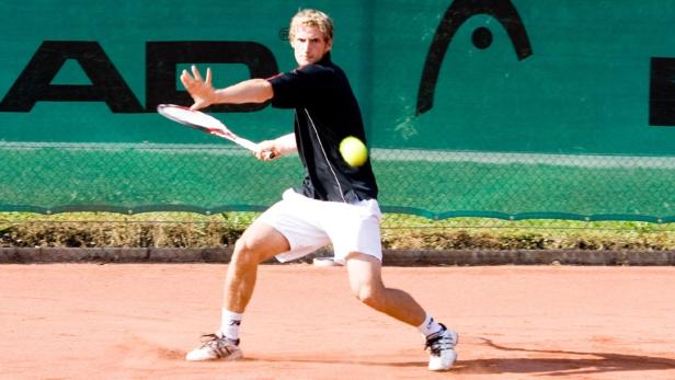 Ein Tennisspieler schlägt einen gelben Tennisball auf einem Sandplatz.