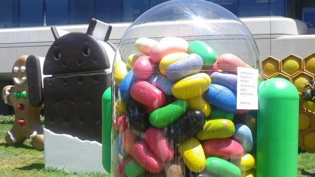 Skulpturen von Android-Figuren und einem Behälter voller bunter Jelly Beans auf einer Rasenfläche.
