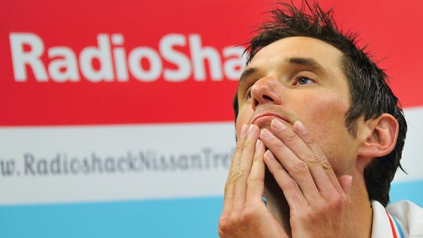 Ein Mann hält seine Hände vor das Gesicht, im Hintergrund ein RadioShack-Logo.