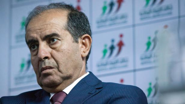 Ein Mann im Anzug vor einer Wand mit einem Logo.