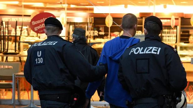 Polizisten führen eine Person in einem blauen Hoodie ab.