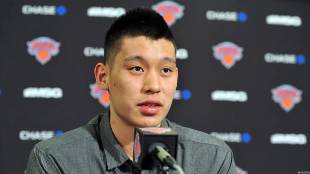 Ein Mann mit kurzem, dunklem Haar spricht vor einem Hintergrund mit Logos der New York Knicks und Chase Bank.