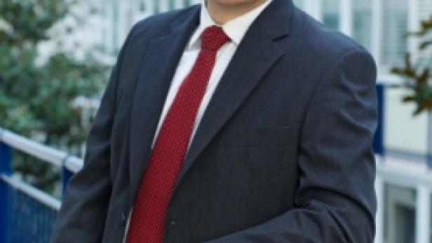 Ein Mann mit Brille, Anzug und roter Krawatte lehnt an einem Geländer.