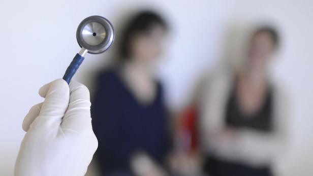 Eine Hand in einem weißen Handschuh hält ein Stethoskop vor zwei Patientinnen.
