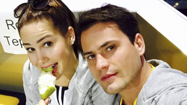 Eine Frau isst einen Apfel, während ein Mann in die Kamera schaut.