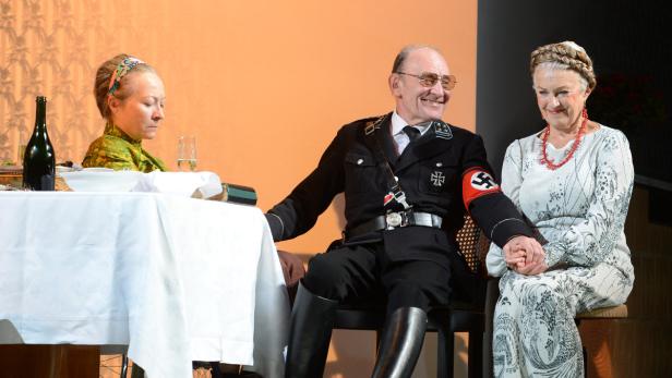 Ein Mann in Nazi-Uniform sitzt am Tisch und hält die Hand einer Frau.