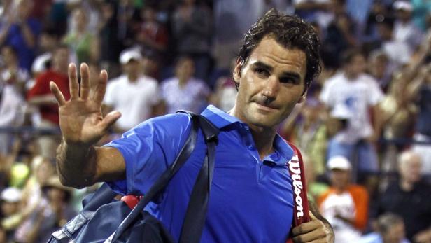 Roger Federer winkt mit einer Tennistasche über der Schulter.