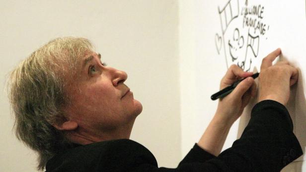 Ein Mann zeichnet eine Karikatur mit der Aufschrift „Alliance Française“ auf eine weiße Wand.