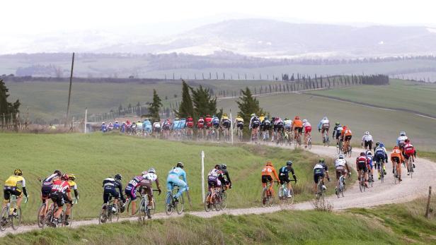 Eine Gruppe von Radfahrern fährt auf einer unbefestigten Straße durch eine hügelige Landschaft.