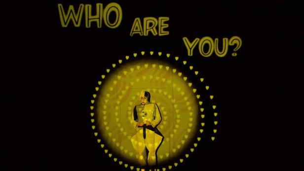 Eine Person sitzt vor einem gelben, kreisförmigen Muster mit der Aufschrift „Who are you?“.