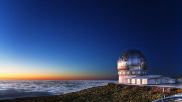 Ein Observatorium steht auf einem Hügel über den Wolken bei Sonnenaufgang.