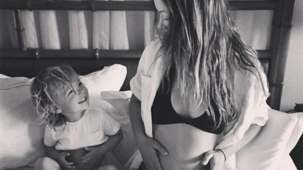 Eine schwangere Frau sitzt mit ihrem kleinen Sohn im Bett.