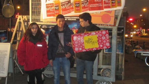 Drei Jugendliche stehen vor einem Stand der Young Caritas mit einer Geschenkbox.