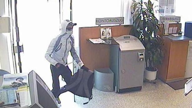 Eine maskierte Person betritt mit einer Tasche eine Bankfiliale.