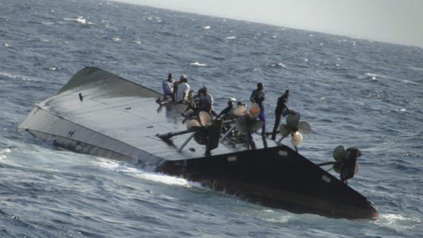 Mehrere Personen befinden sich auf einem gekenterten Boot im Meer.