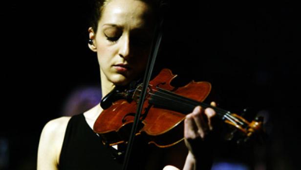 Eine junge Frau spielt auf einer dunklen Bühne Violine.
