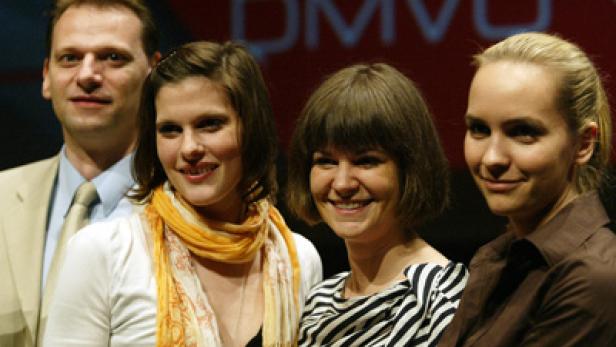 Eine Gruppe von vier Personen posiert vor einem roten Hintergrund mit dem Schriftzug „DMVÖ“.