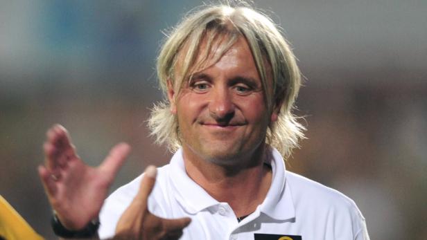 Ein Mann mit blonden, schulterlangen Haaren lächelt.