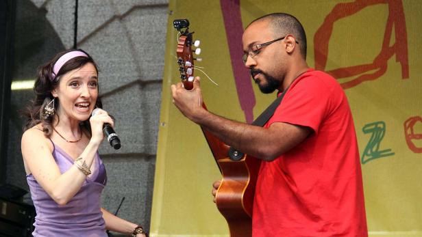 Eine Sängerin mit Mikrofon und ein Gitarrist treten auf einer Bühne auf.