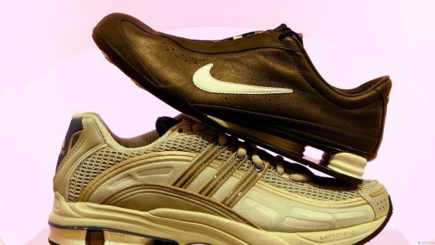 Ein schwarzer Nike-Schuh liegt auf einem beigen Adidas-Schuh.