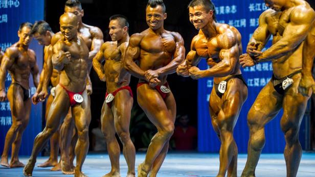 Eine Reihe von Bodybuildern posiert auf einer Bühne während eines Wettkampfs.