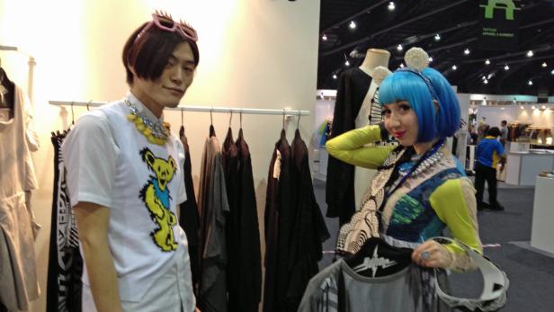 Zwei Personen posieren auf einer Textilmesse vor einem Kleiderständer.
