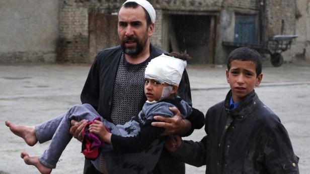 Ein Mann trägt ein verletztes Kind, während ein anderer Junge daneben steht.