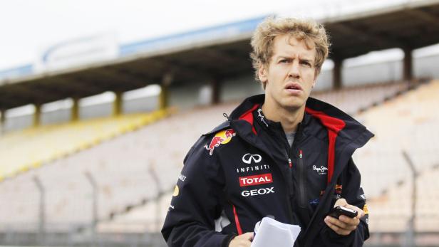 Sebastian Vettel in seiner Rennjacke mit Handy auf einer Tribüne.