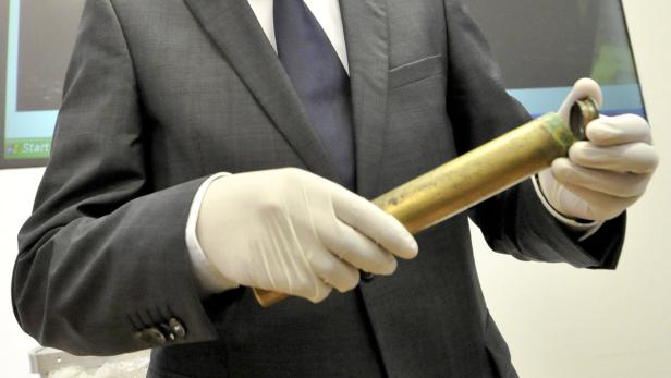 Eine Person in einem Anzug und Handschuhen hält einen goldenen Zylinder.