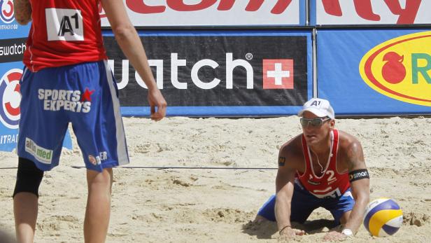 Ein Beachvolleyballspieler kniet im Sand, bereit für den Aufschlag.