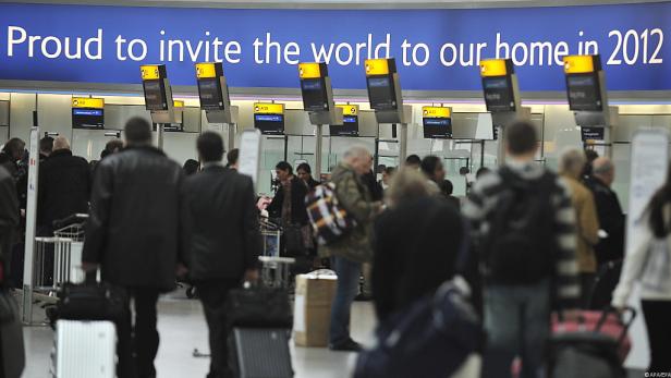 Menschen stehen an Check-in-Schaltern auf einem Flughafen.