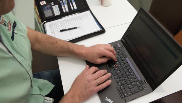 Ein Mann tippt auf einem schwarzen ThinkPad Laptop an einem weißen Tisch.