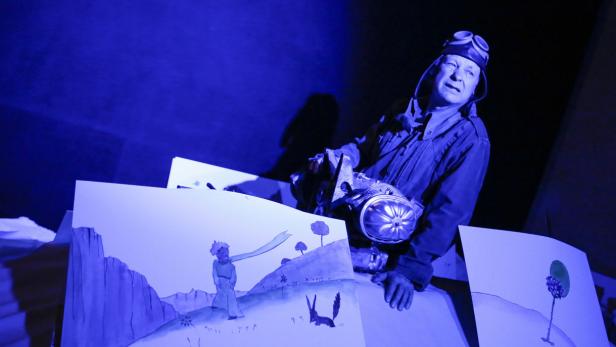 Ein Mann mit Fliegerbrille inszeniert „Der kleine Prinz“ mit Zeichnungen.