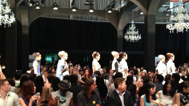 Models präsentieren Mode auf einem Laufsteg vor einem Publikum.