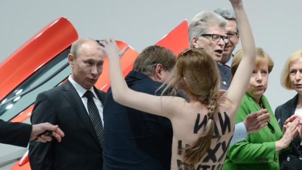 Eine Aktivistin protestiert mit nacktem Oberkörper vor Wladimir Putin und Angela Merkel.