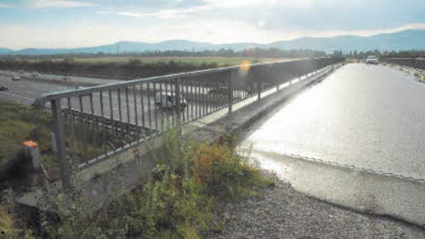 Eine Brücke über eine Autobahn mit Feldern und Bergen im Hintergrund.
