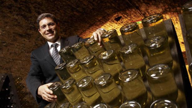 Ein Mann im Anzug präsentiert Flaschen, die in einem Weinkeller lagern.