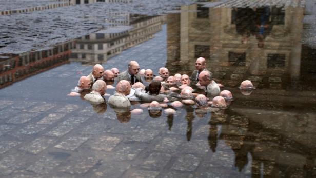 Eine Gruppe von Skulpturen, die in einer Wasserpfütze auf einem gepflasterten Platz stehen.