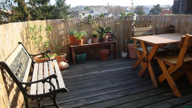 Eine Terrasse mit Holzboden, einer Bank, einem Tisch und vielen Pflanzen in Töpfen.