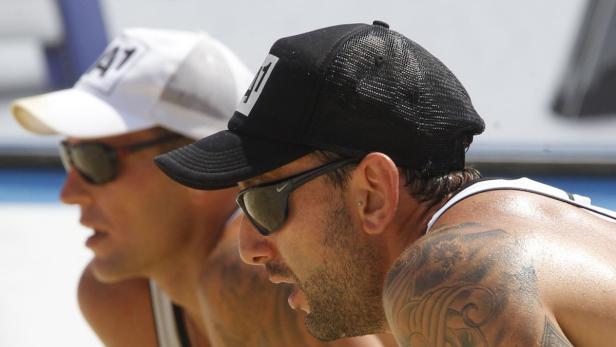 Zwei Beachvolleyballspieler mit Sonnenbrillen und Kappen auf dem Spielfeld.