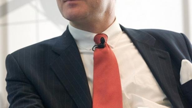 Ein Mann mit Brille, Anzug und roter Krawatte sitzt und schaut nach rechts.