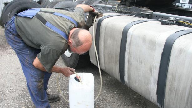 Ein Mann befüllt einen Kanister mit Flüssigkeit aus dem Tank eines Lastwagens.