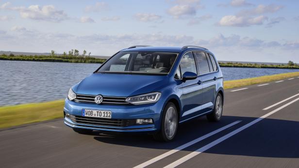 Ein blauer VW Touran fährt auf einer Landstraße entlang eines Sees.