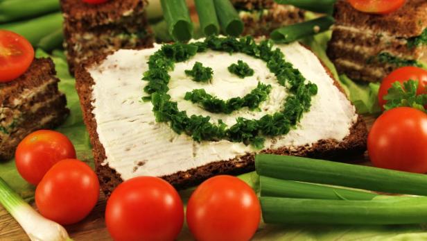 Ein Brot mit Frischkäse und einem lächelnden Gesicht aus Schnittlauch verziert.