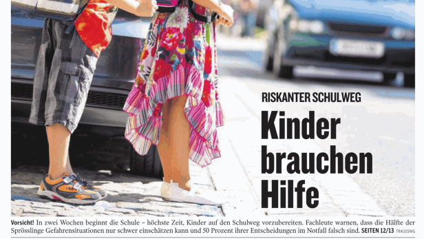 Zwei Kinder mit Schulranzen stehen an einer Straße.