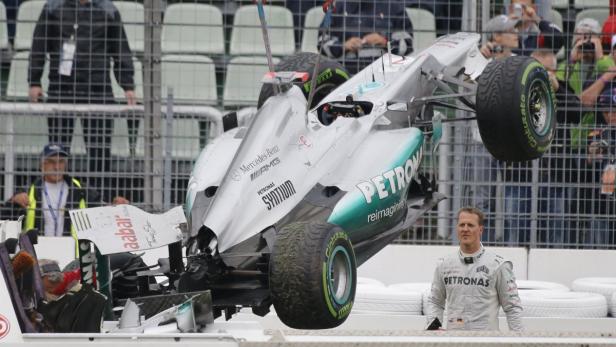 Ein beschädigter Mercedes-Benz Formel-1-Wagen wird von der Strecke gehoben, Michael Schumacher steht daneben.