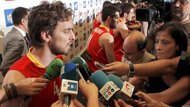Ein Basketballspieler im roten Trikot wird von Reportern interviewt.